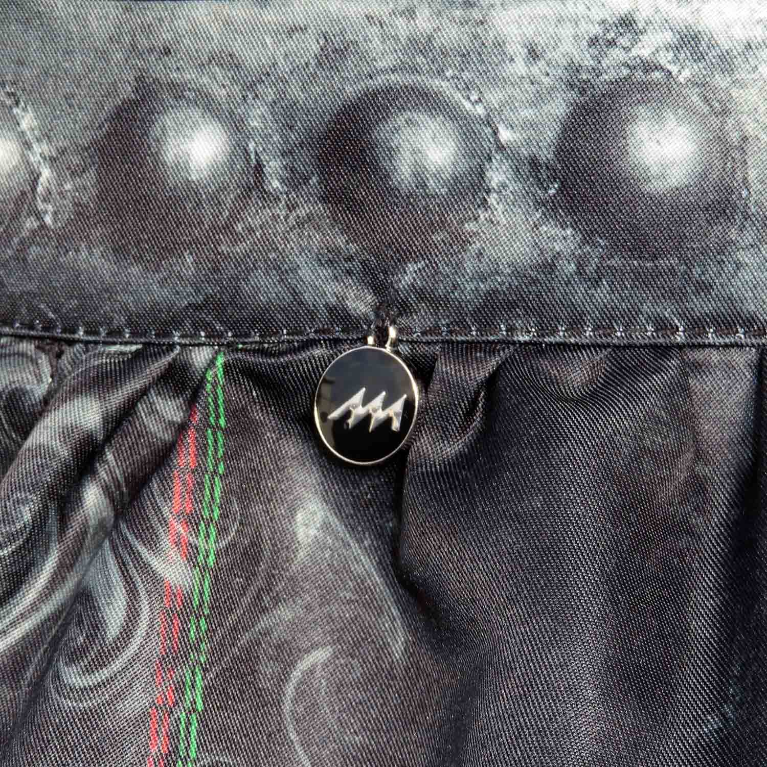 Dirndlschürze "Alpenrock" in Midi von Alexandra Maxa - Detailansicht von dem Schürzenbund mit Nieten-Optik und einem Metall-Logo-Anhänger