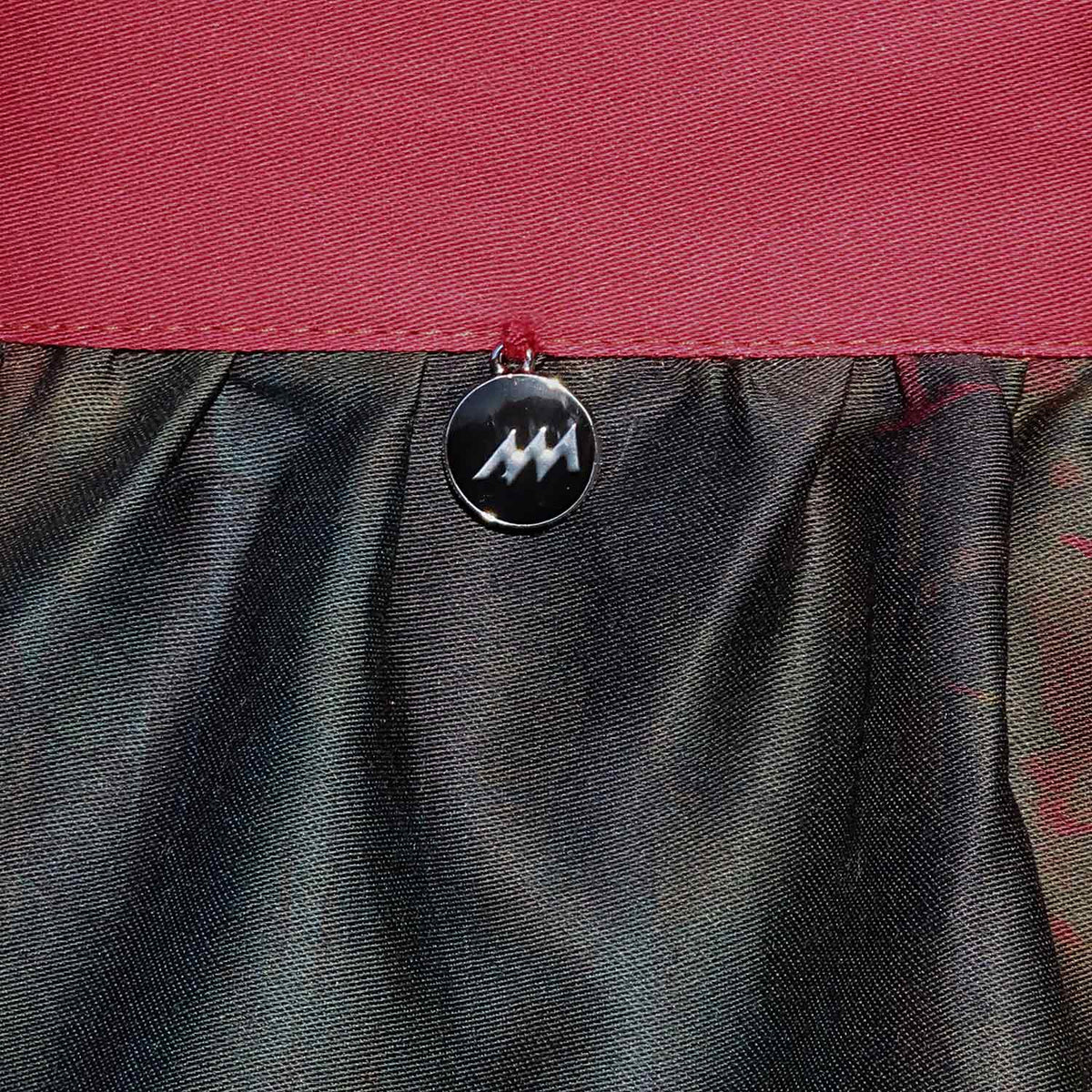 Dirndlschürze "Grossstadt-Dschungel" in Midi von Alexandra Maxa TD-D07539-19 Detailansicht vom Schürzenbund mit Metall-Logoanhänger